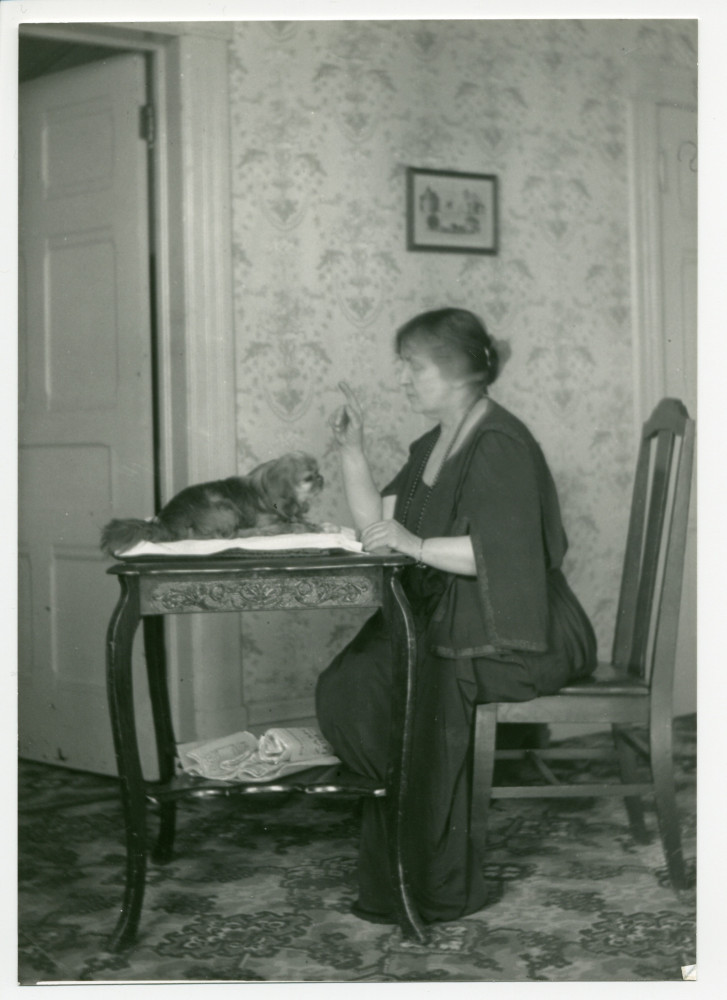 Photographie d'Hélène Paderewska parlant à son chien Ping, installé sur une table dans sa chambre à coucher de Riond-Bosson