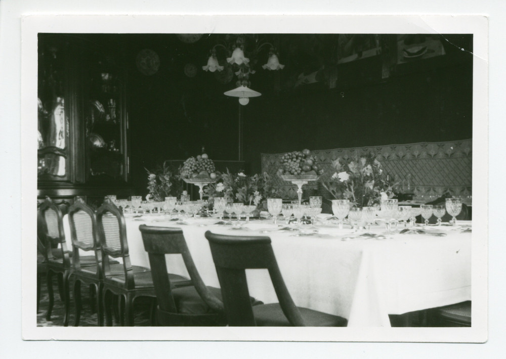 Photographie de la salle à manger de Riond-Bosson, avec la table mise pour un dîner de gala (4 verres en cristal: un pour l'eau, un pour le vin blanc avec le poisson, un pour le vin rouge avec la viande, un pour le champagne avec le dessert