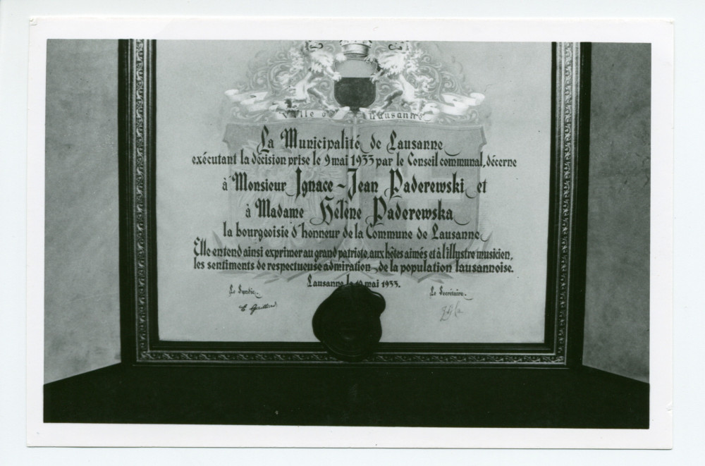 Photographie de détail de l'encadrement (reproduction?) du diplôme de citoyen d'honneur décerné à Paderewski par la Ville de Lausanne, exposé sur un piano à queue du salon de Riond-Bosson