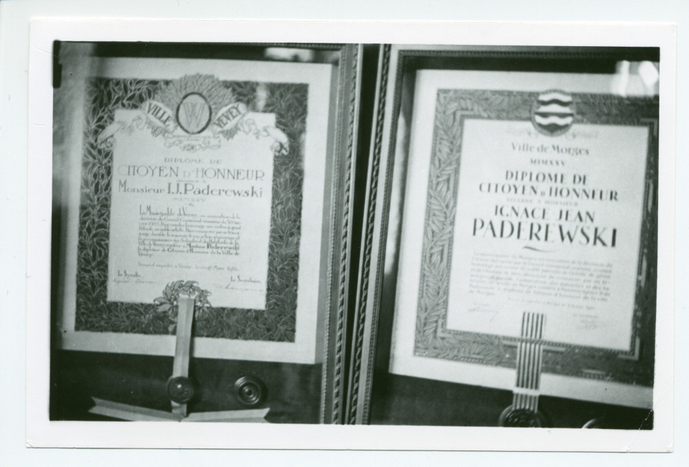 Photographie des encadrements (reproductions?) des diplômes de citoyen d'honneur décernés à Paderewski par les Villes de Morges et de Vevey, exposés sur un piano à queue du salon de Riond-Bosson