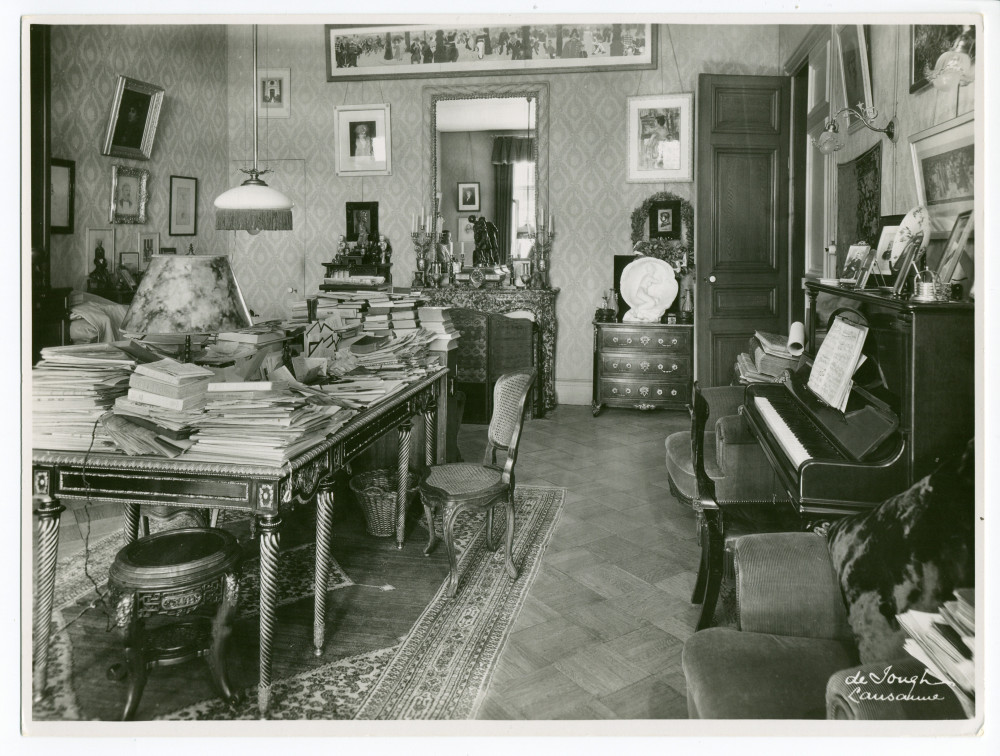 Photographie du studio de Paderewski à Riond-Bosson réalisée par l'Atelier de Jongh à Lausanne, avec à gauche son bureau recouvert de documents et à droite le piano droit