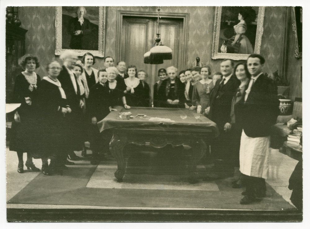 Photographie de Paderewski distribuant des cadeaux aux employés de Riond-Bosson autour de la table de billard, dans le hall, avec en arrière-fond les portraits d'Ignace et de Hélène Paderewski par Charles Giron, lors du réveillon 1930