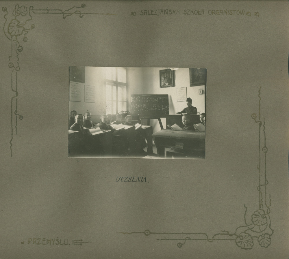 Album de présentation de l'Oratoire (école) salésien pour organistes de Przemysl, réalisé à l'occasion de l'année scolaire 1922-1923 – page 17: photographie d'une salle de classe avec élèves, professeur et tableau noir avec musique