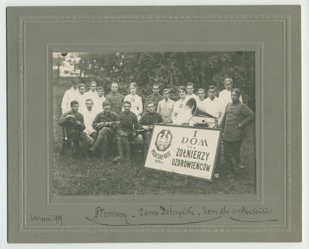 Photographie de soldats convalescents (dont deux jouant de la guitare) en compagnie d'infirmières dans le jardin de la maison de convalescence de la Croix Blanche polonaise à Plomiany, avec pancarte de l'établissement et gramophone, en septembre 1919