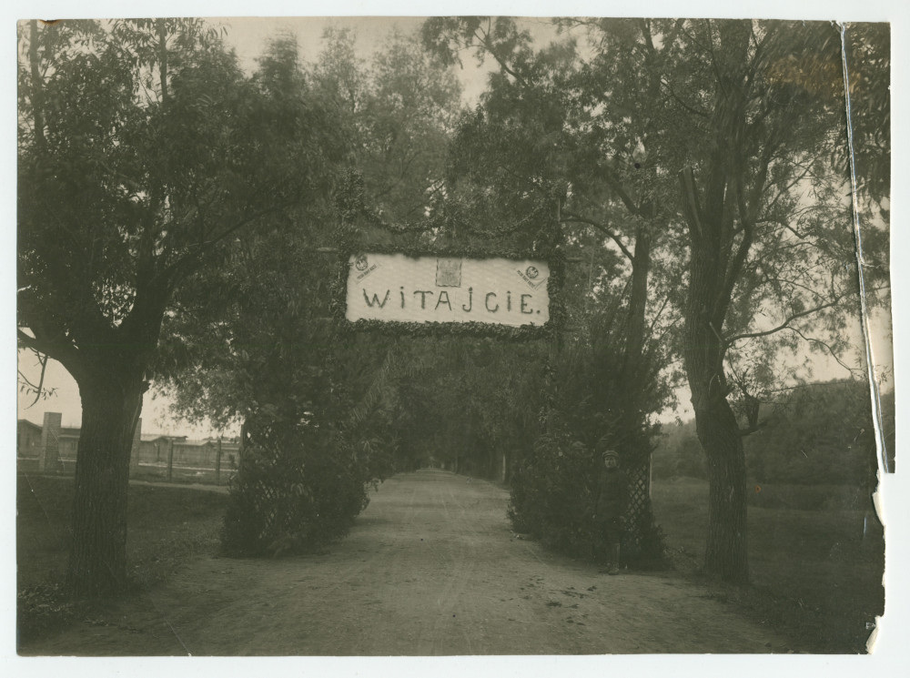 Photographie du panneau de bienvenue réalisé par des prisonniers de guerre au point d'alimentation de la Croix Blanche polonaise à Deblin, ville de la voïvodie de Lublin, dans l'est de la Pologne – avec légende manuscrite et nom du photographe au verso