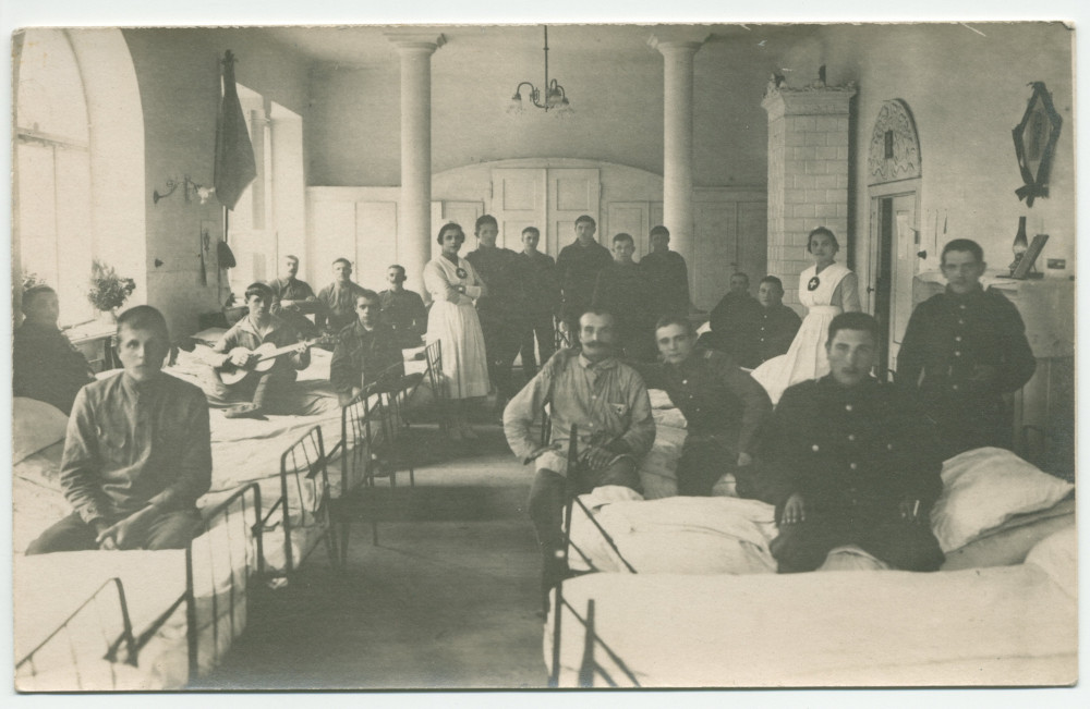 Photographie de soldats convalescents assis sur leur lit dans une chambre d'hôpital tenu par la Croix Blanche polonaise (l'un jouant de la guitare) – tirage carte postale