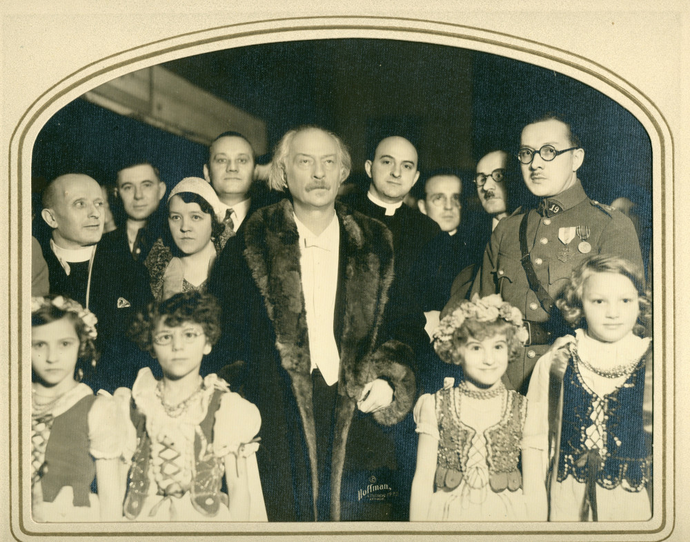 Photographie de Paderewski posant en manteau de fourrure au milieu d'enfants (en costume traditionnel polonais?), de militaires et d'hommes d'église, en marge d'un récital donné à Détroit en 1932, dans une luxueuse fourre cartonnée du Hoffman Studio