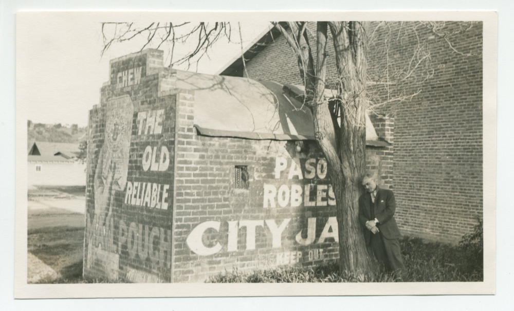 Photographie de la prison de Paso Robles, en Californie, avec au premier plan un homme adossé contre un arbre