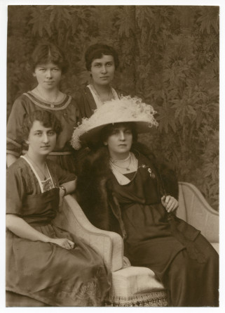 Photographie d'Hélène Paderewska, avec chapeau blanc et collier de perles, assise entourée de trois jeunes femmes dont sa secrétaire Mlle Hélène Lübke (debout à gauche), réalisée probablement le 5 février 1920