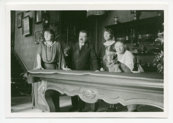 Photographie d'Hélène Gorska avec (de gauche à droite) le Dr Orowski, Mme Vaslav Gorska (sa belle-fille), Antonina Wilkonska et le chien Ping, dans le hall de Riond-Bosson, avec la table de billard et au fond l'escalier menant aux appartements privés