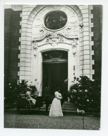 Photographie d'Hélène Paderewska tenant son chien Ping dans ses bras devant l'entrée principale de Riond-Bosson, avec à ses côtés un landau conduit par un homme non identifié
