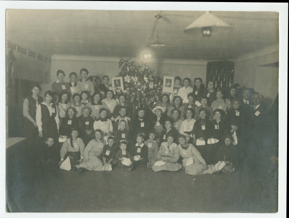 Photographie de groupe (enfants et adultes munis de l'écusson de la Croix Blanche polonaise) à l'occasion d'une fête de Noël organisée le 21 décembre 1920 au numéro 1 de la rue Sikorski (ville?) en hommage (?) à Hélène Paderewska