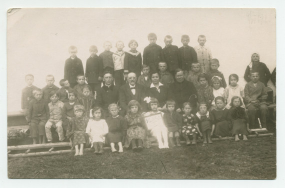 Photographie d'une classe de première année (sans doute financée par la Croix Blanche polonaise) avec enseignants, en 1925 – avec légende manuscrite difficile à lire au verso («Madame Moriwe à Deblin?)
