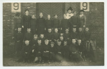 Photographie d'enfants en uniforme noir posant devant le mur en briques d'une crèche de la Croix Blanche polonaise, encadrés par quatre dames – tirage carte postale